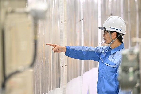 ②Uchino pointing at and checking hydrogen production equipment