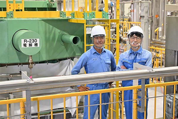 水素製造設備の電解槽前に立つ旭化成の作業を着た技術者2名